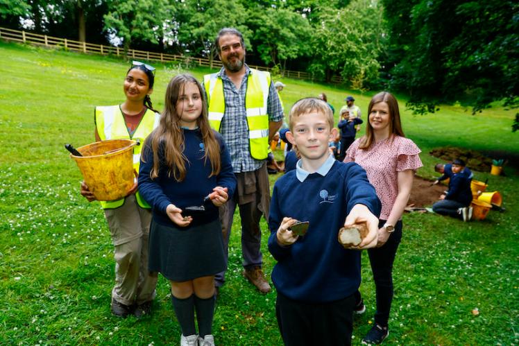School children, under a tree, with their teachers, showing objects found during their archaeological dig.