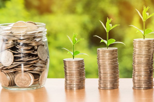 Image shows a jar filled with coins, and two stacks of coins beside it.