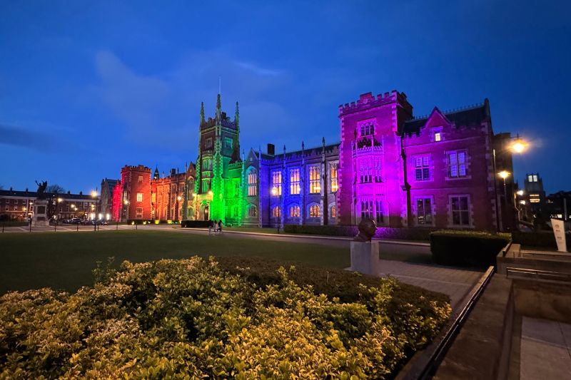 Side of the Lanyon Building light up in rainbow colours against a dark night sky.