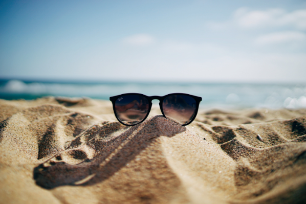 Image shows a pair of sunglasses on a sandy beach