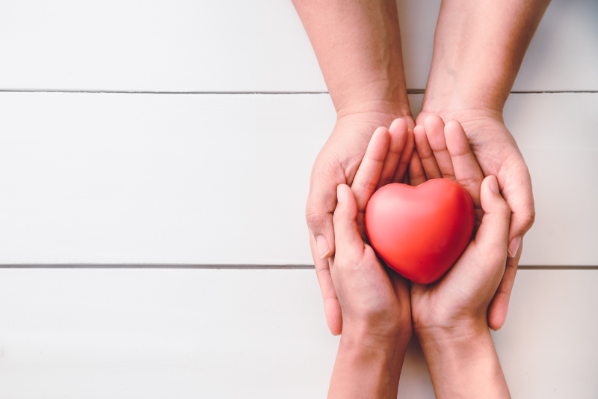 Image shows two pairs of hands holding a red heart