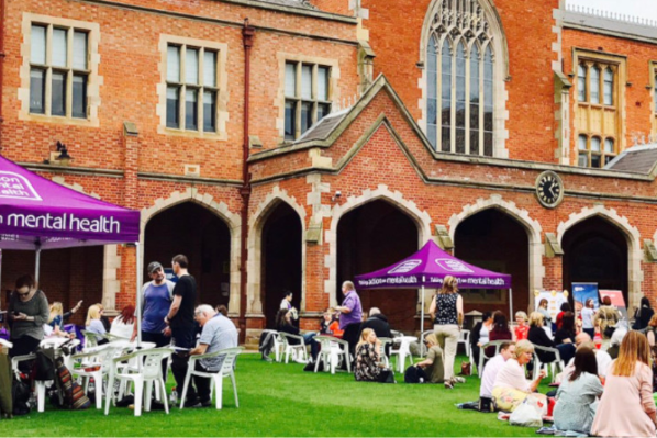 Image shows the Mental Health Awareness picnic taking place on the lawn in the Quad, with staff eating lunch at picnic tables