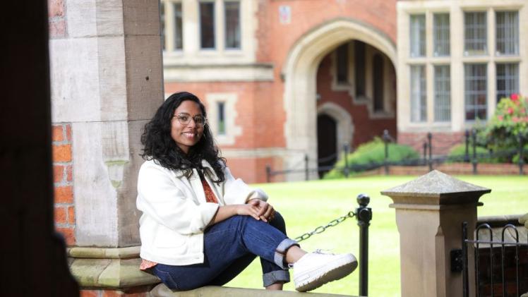 female international student sitting in Queen's quad area in sunshine with laptop