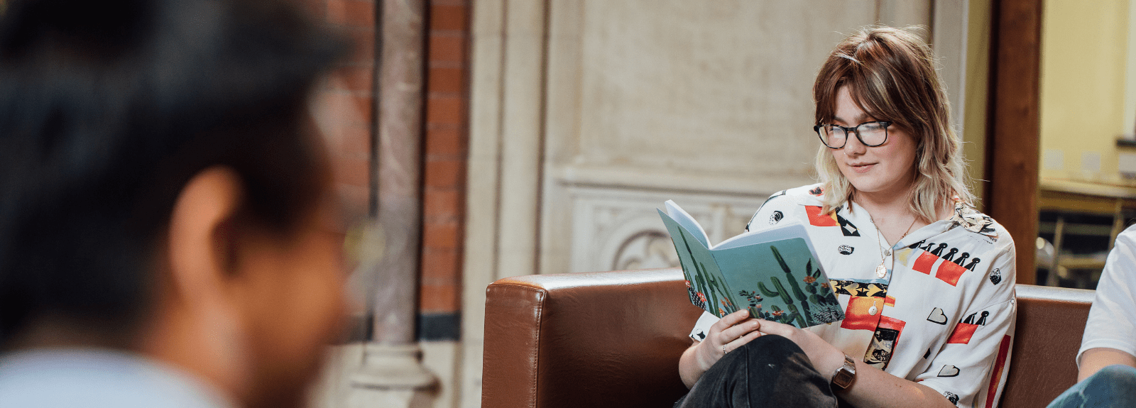 Student in the Graduate School Social Space area, sitting on a sofa reading a book