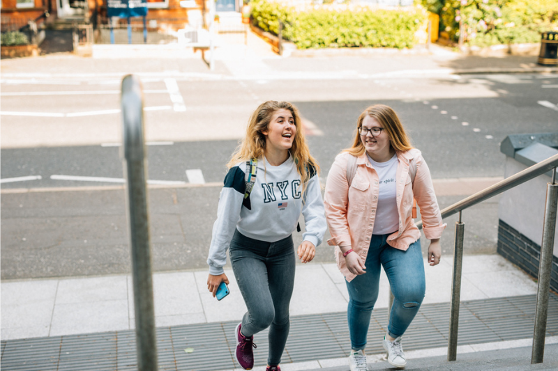 two female students walking up some steps outside whilst chatting