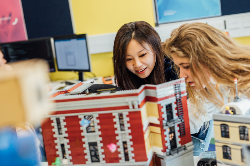 two female students looking at a tiny building structure