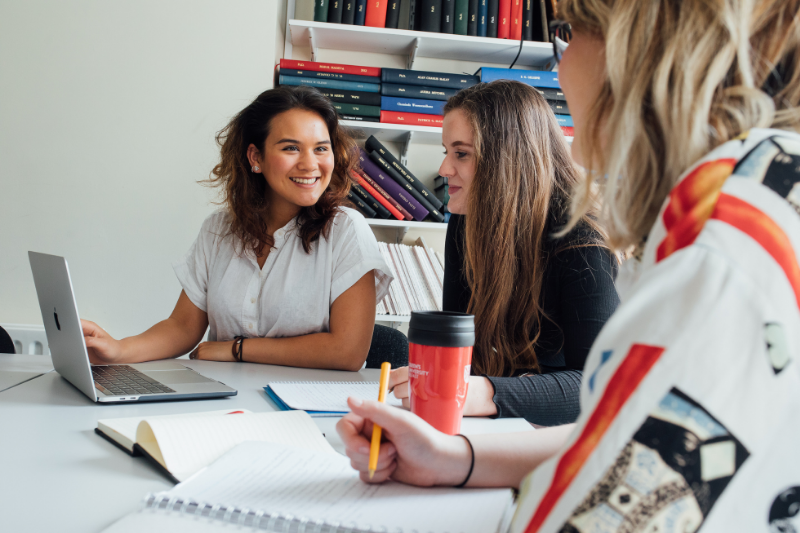 female students sitting in a university room around a small table chatting