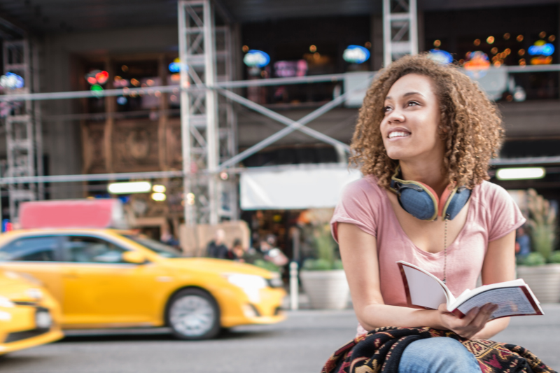 female student sitting on a bench in New York with a yellow cab in the background