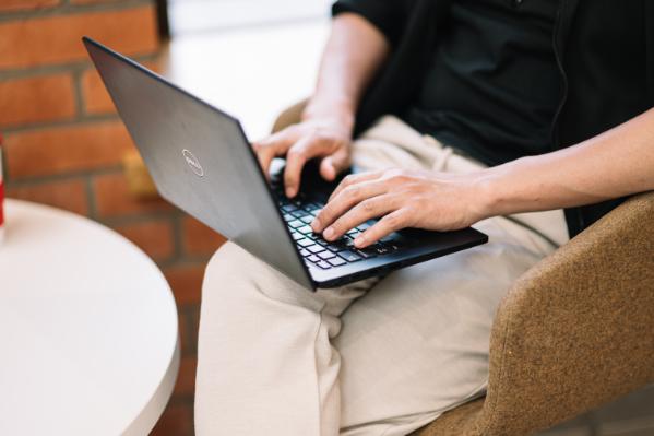 A student typing on their laptop which is resting on their knee.