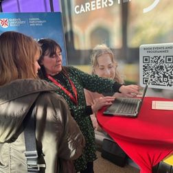 careers consultant talking to a student showing them something on a laptop at autumn fair stall