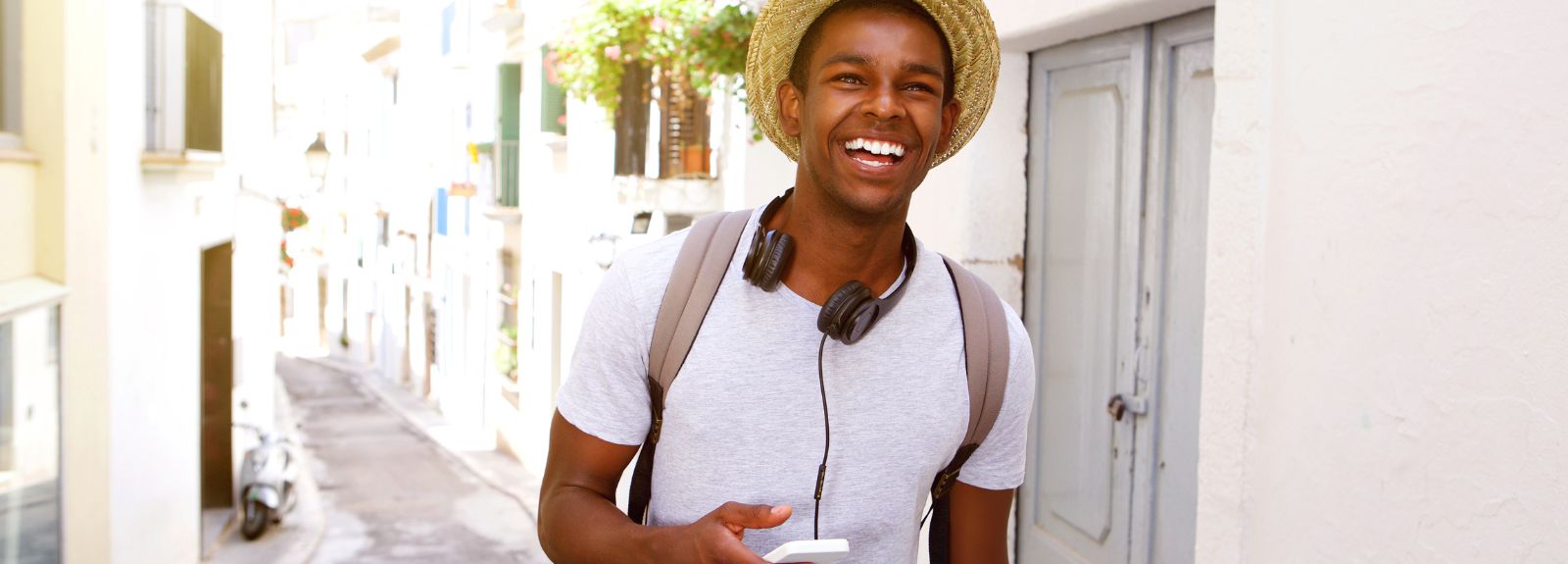 young male wearing a straw hat walking in a town in the sun whilst holding a phone