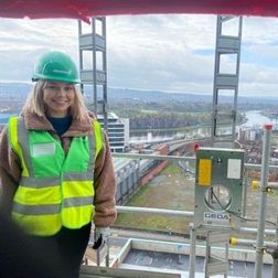 female student in a hard hat standing high up on a platform on a building siteon work experience
