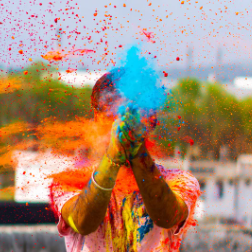 Image shows a man celebrating Holi surrounded by colour