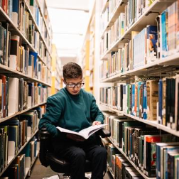Image shows a student with a disability reading a book in the library.