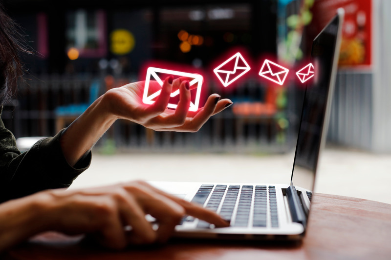 Image shows a person typing on a laptop with red neon 'Email' symbols floating in the air.