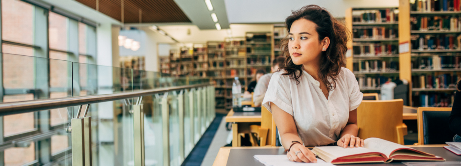 A female student sitting at a desk in a library, thinking