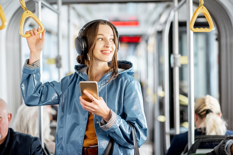 female student standing on a bus with headphones on holding phone