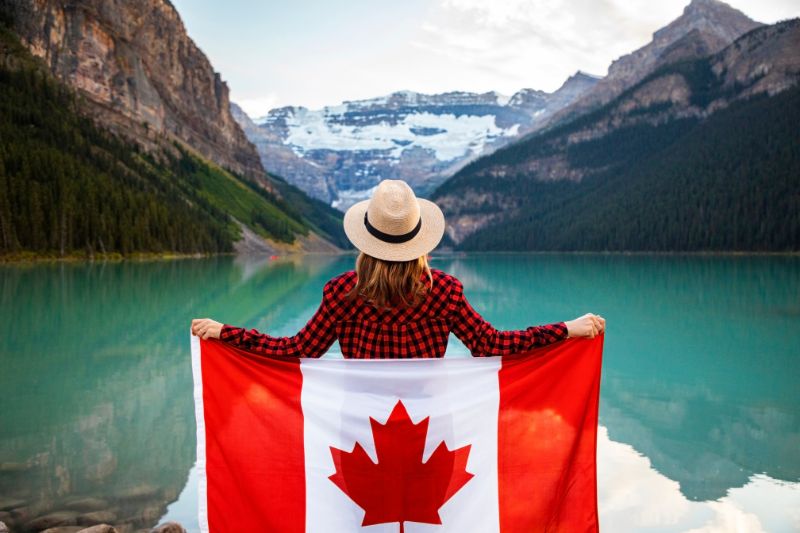 female holding up a Canadian flag standing looking at mountains