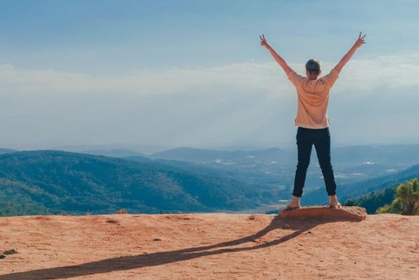student standing on a hill top with arms stretched up to the sky