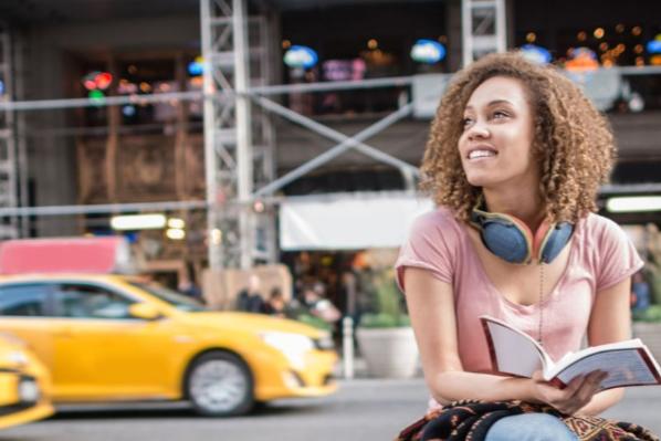 student sitting outside in New York as yellow cab rides past on road