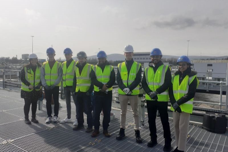 student standing in a group outdoors at a company's premises in hard hats and high vis jackets