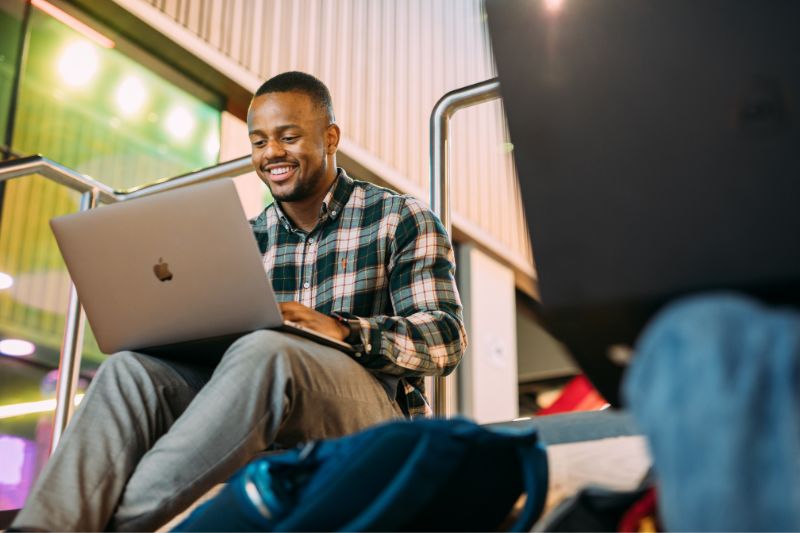 male student sitting on a staircase using a laptop