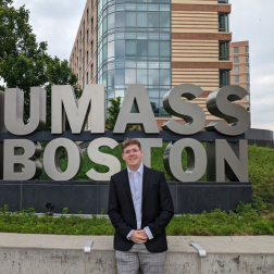 student standing at UMass Boston sign