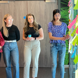 three female students standing as part of a group presenting to other students