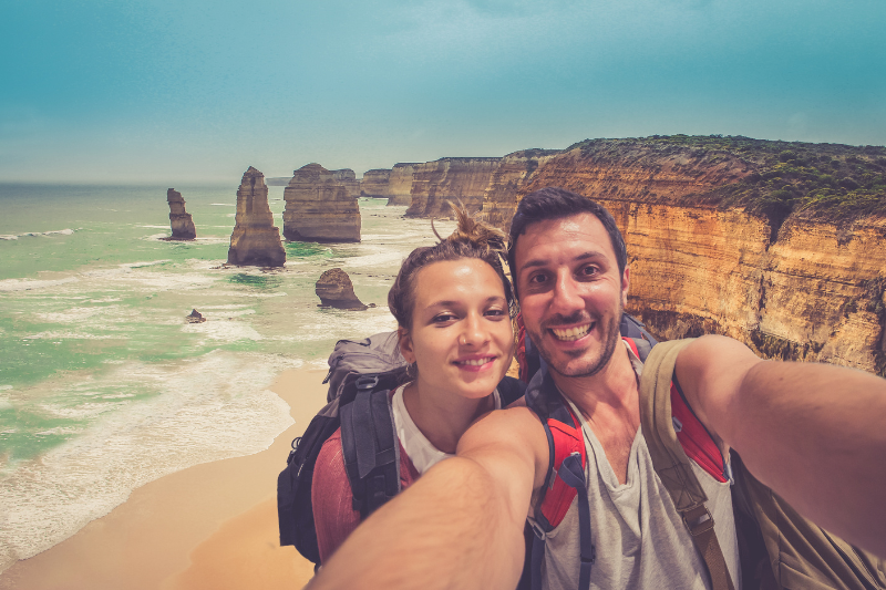 young male and female standing together taking a selfie on a beach