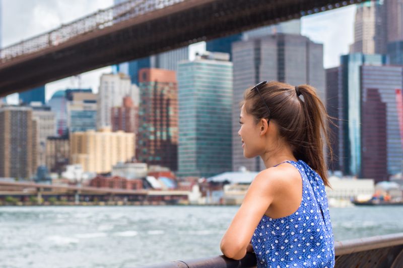 student standing staring at a river with bridge above