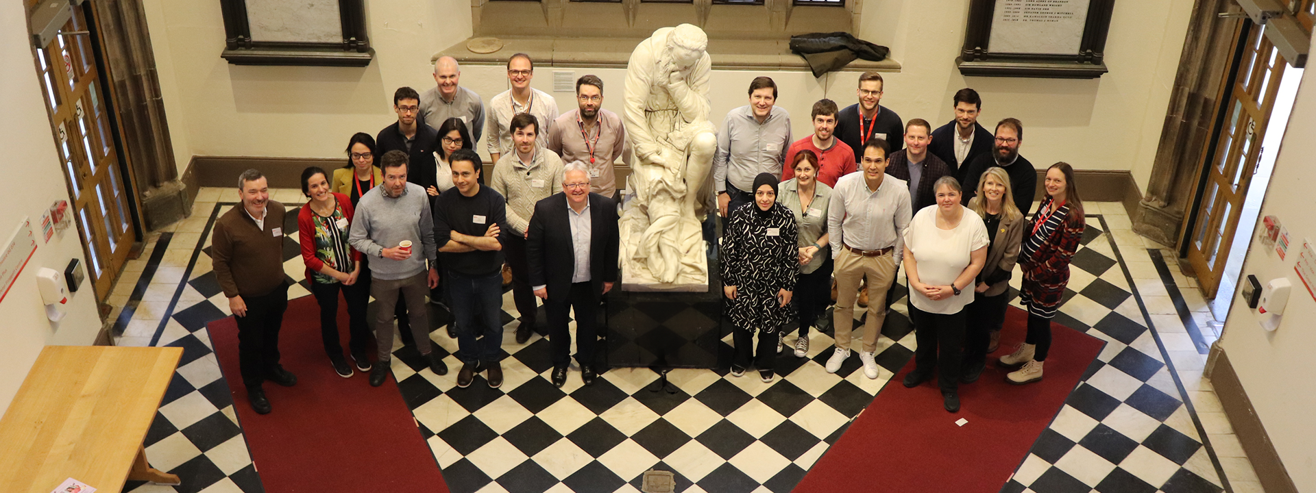 Several members of the QUB Fellowship Academy standing in the Black and White hall, beside a statue looking up.