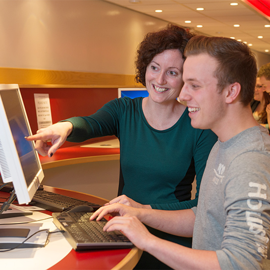 member of staff assisting student using a computer