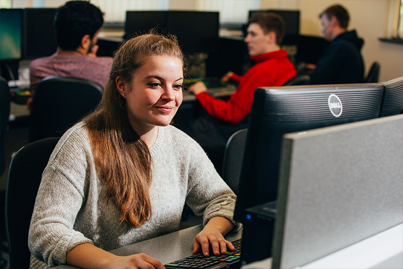 Female student using a computer in the First Derivatives Trading Room with other students working in the background