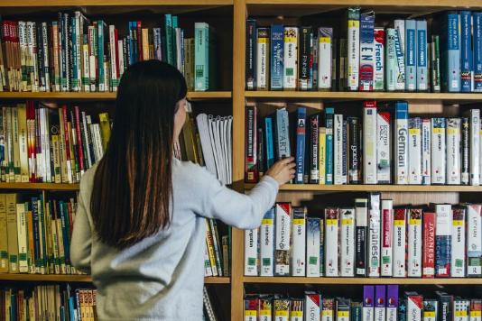 student removing a French language CD from a shelf of learning materials in the QUB Language centre