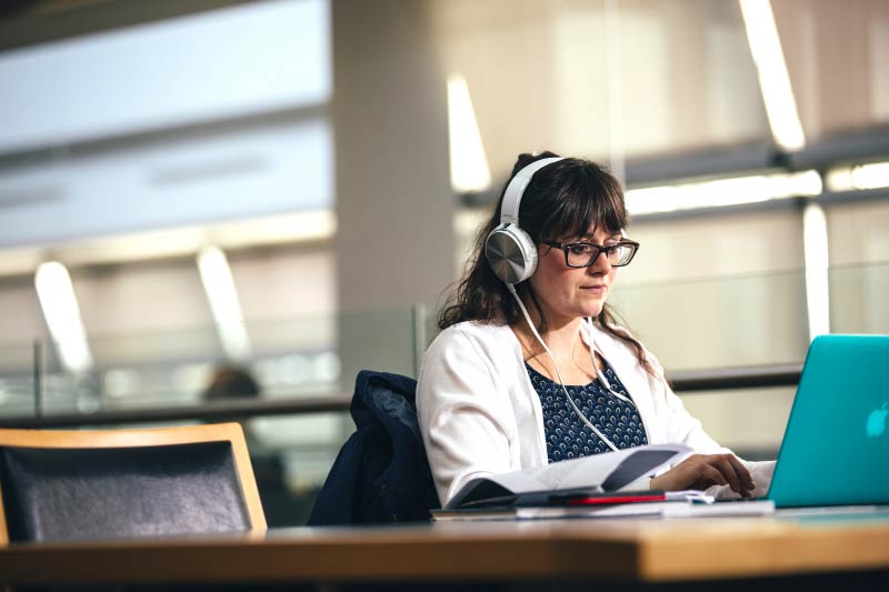 close up of female student wearing headphones and studying on blue laptop