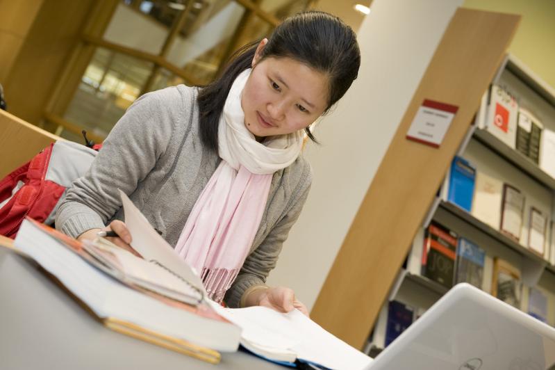 Female student studying with books and laptop in the McClay Library