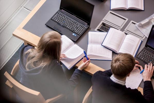 Overhead of 2 students studying with laptops and books in the McClay Library.