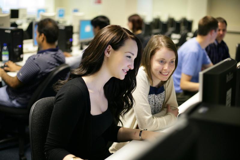 Two female students smiling and using a computer