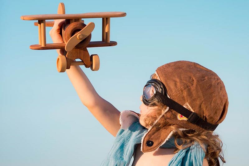 A child wearing goggles and an old fashioned pilots hat playing with a wooden toy plane