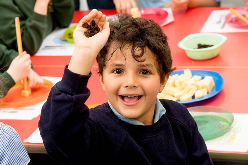 boy in  a school uniform holding a handful of raisins and smiling