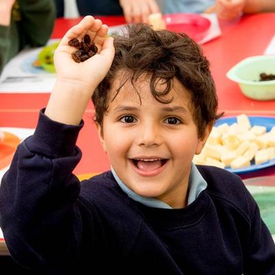 a smiling boy in school uniform holding a handful of raisins