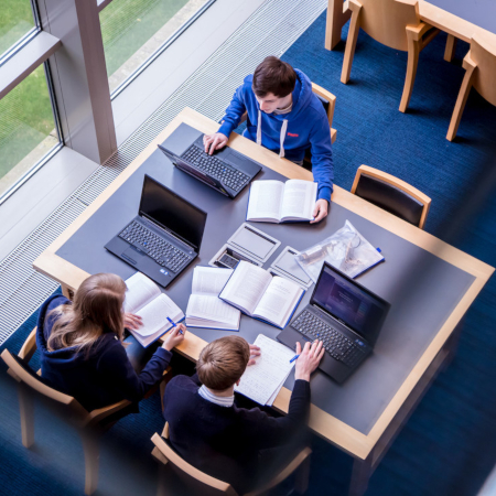 Overhead of students studying with laptops and books in the McClay Library.