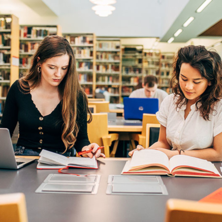 Two female students studying books at a desk in the McClay Library. 