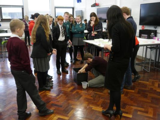 Year 10 pupils from different schools watch to see how much weight their tinfoil boats will hold in a mechanical engineering challenge.