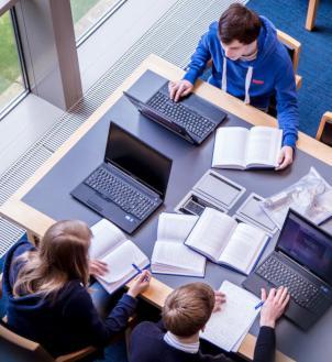 Overhead of 3 students studying with laptops and books in McClay Library