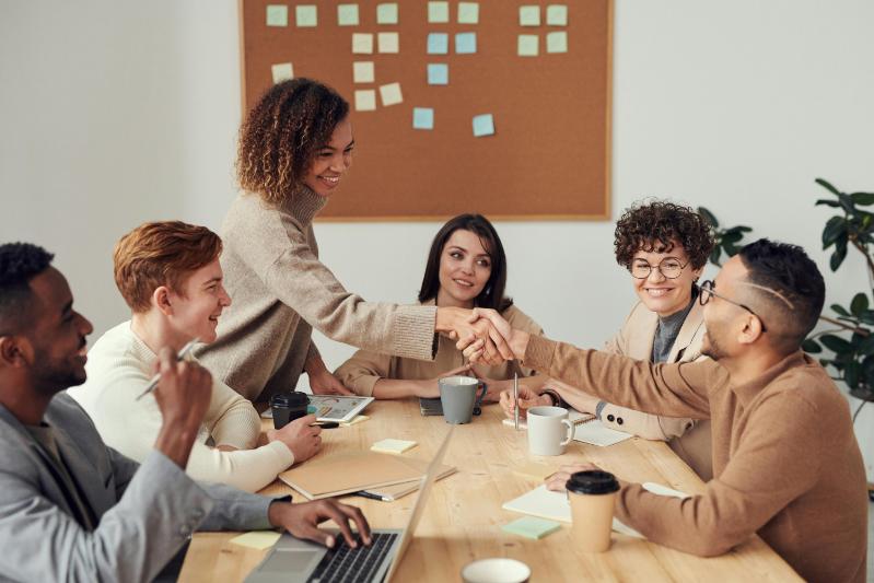 Two people shaking hands around a table with people