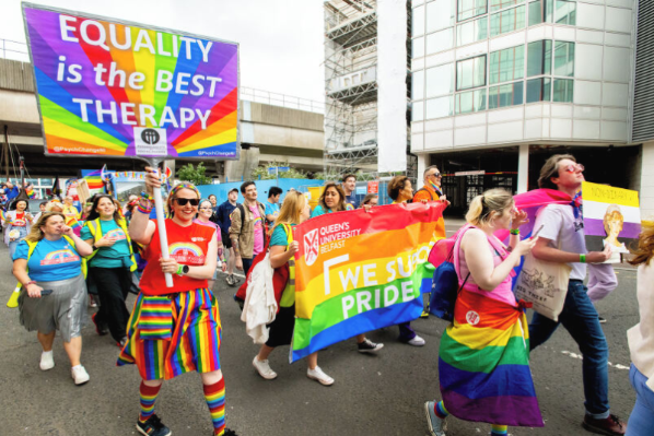 Image shows staff taking part in the Belfast Pride march, holding rainbow banners. One reads: Equality is the best therapy. The other reads: We support pride.