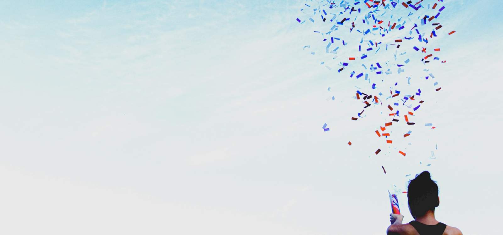 A person celebrates with a confetti popper, firing the confetti into the sky
