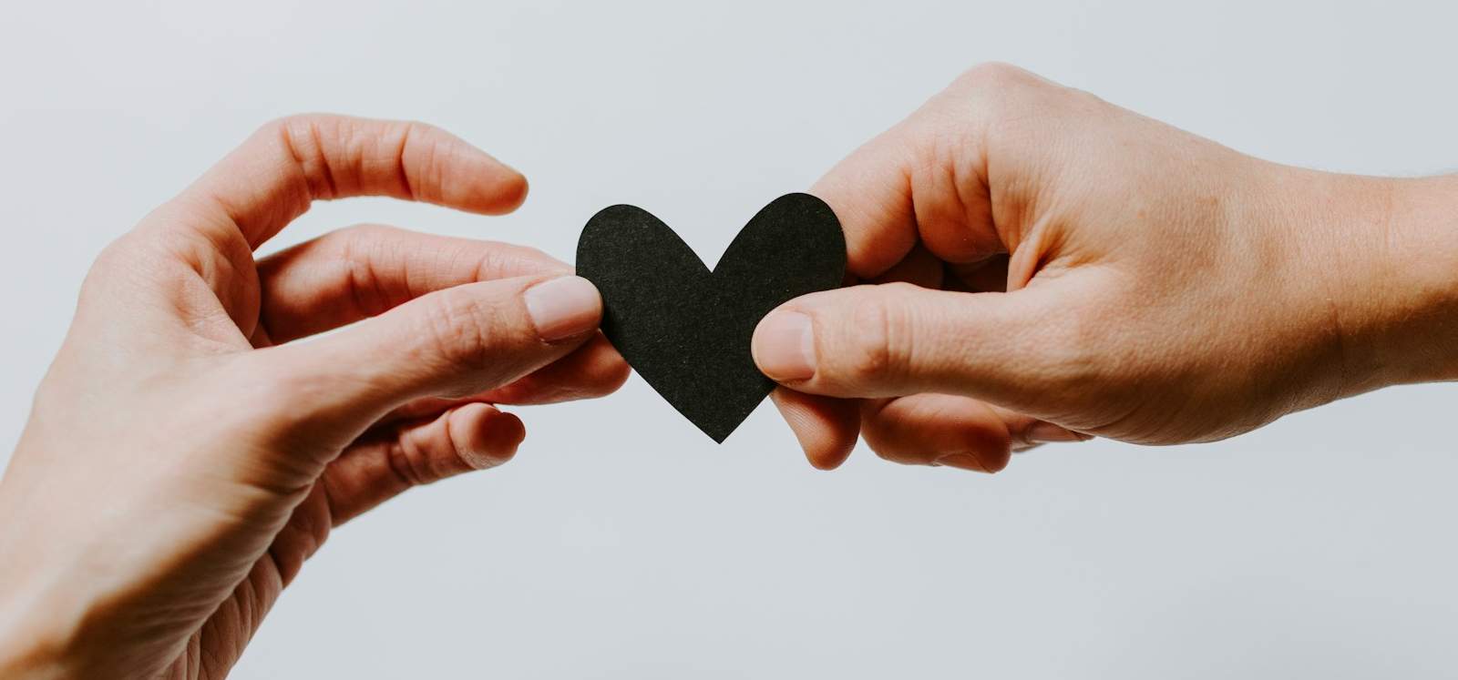 Two hands, each holding an opposite side of a paper heart.