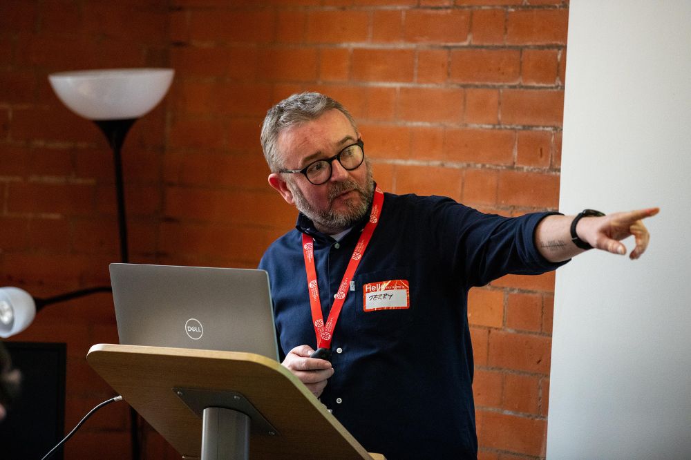 A speaker at the Inclusive Employment Scheme event stands at a podium, gesturing to the right while presenting.